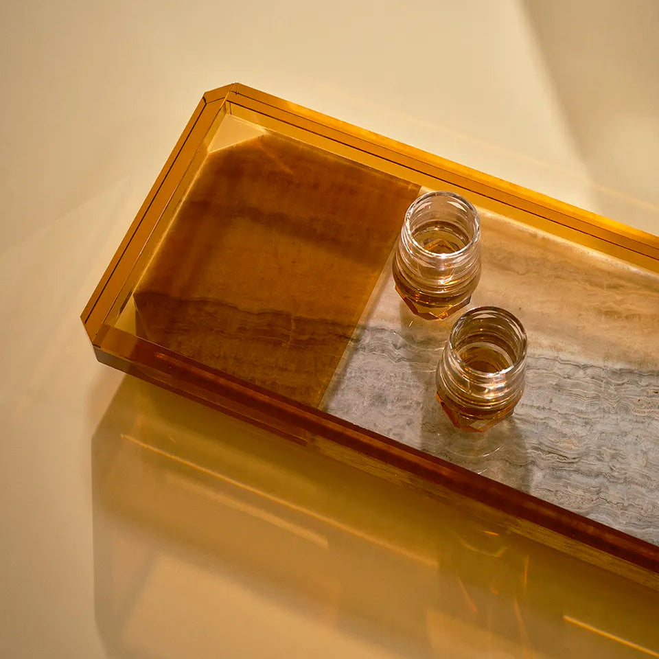 A close-up of the Shadow Tray’s amber and marble textures, with two crystal glasses placed on it, reflecting warm golden light.
