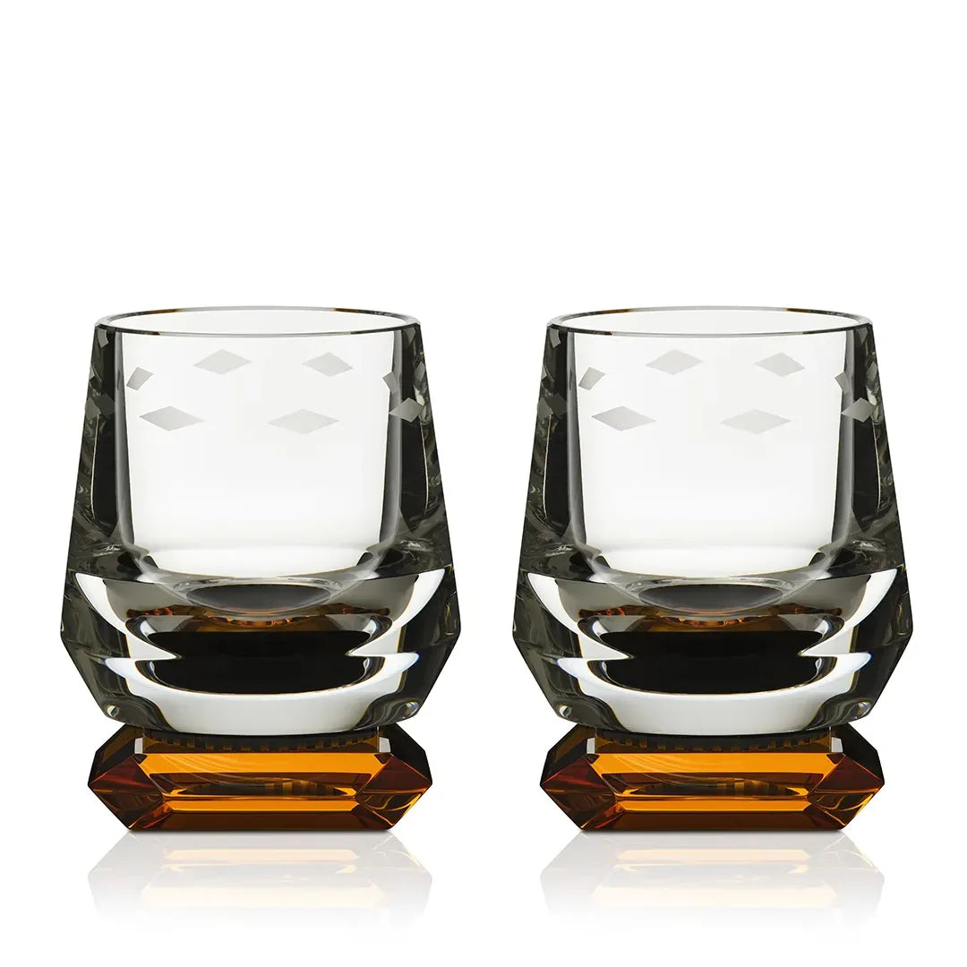 A pair of Whimsy Amber Whisky Glasses with geometric facets and a rich amber base, displayed against a white background.