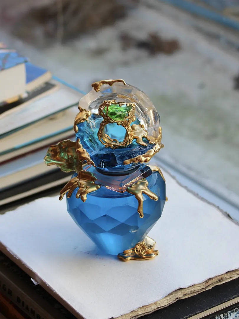 A luminous blue crystal sculpture adorned with 18ct gold-plated silver detailing and green accents, exuding elegance.