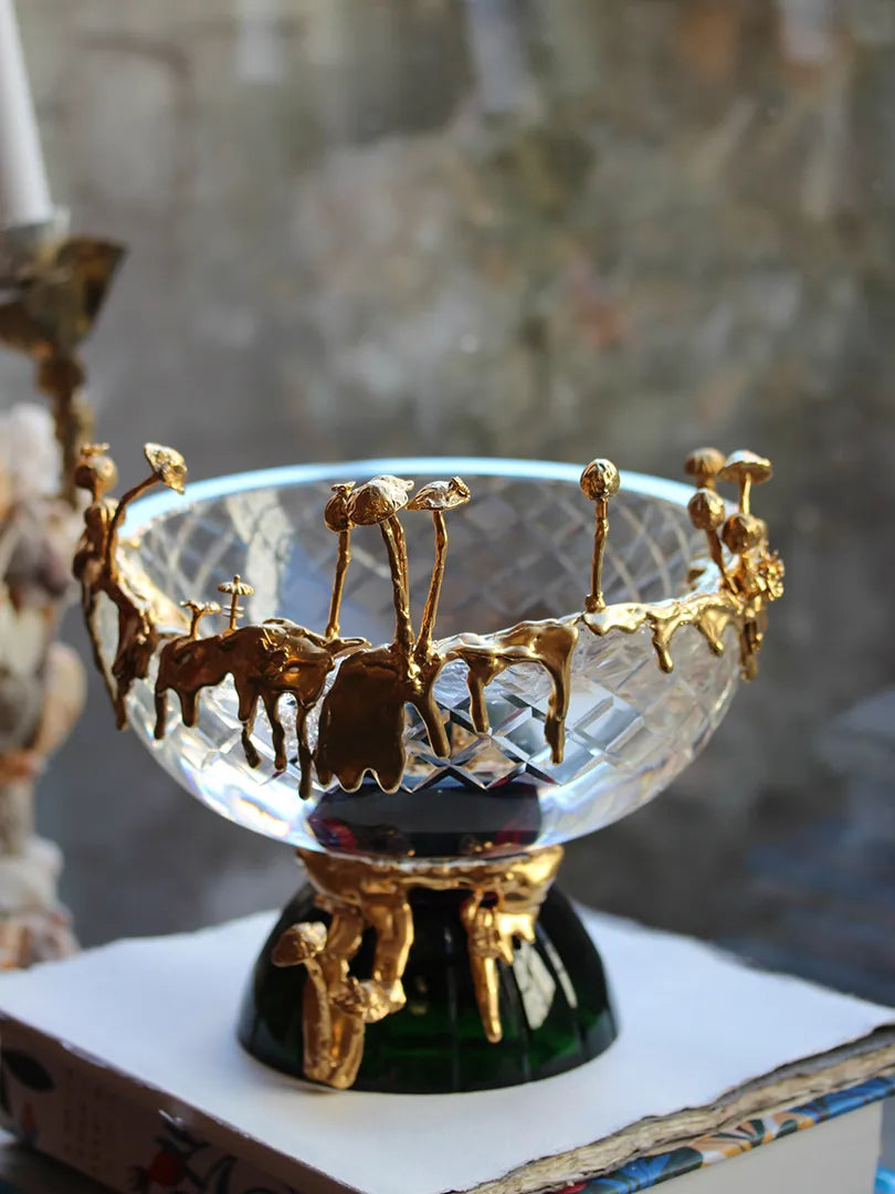 A crystal bowl named "Mycelium Bowl," featuring an intricate design of 18-carat gold-plated silver resembling organic mycelium growth. The bowl is clear crystal with a textured, faceted surface and is adorned with golden drips and delicate mushroom-like forms. It sits on a sturdy emerald green base with burgundy accents, adding depth and elegance.